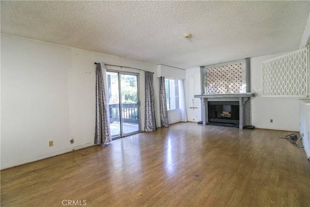 unfurnished living room featuring a glass covered fireplace, baseboards, a textured ceiling, and wood finished floors