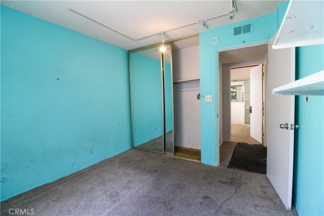 unfurnished bedroom featuring a closet, visible vents, track lighting, and carpet