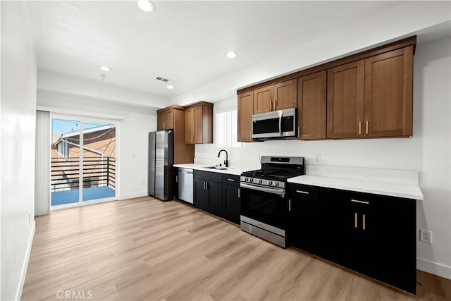 kitchen with light countertops, light wood finished floors, recessed lighting, appliances with stainless steel finishes, and a sink
