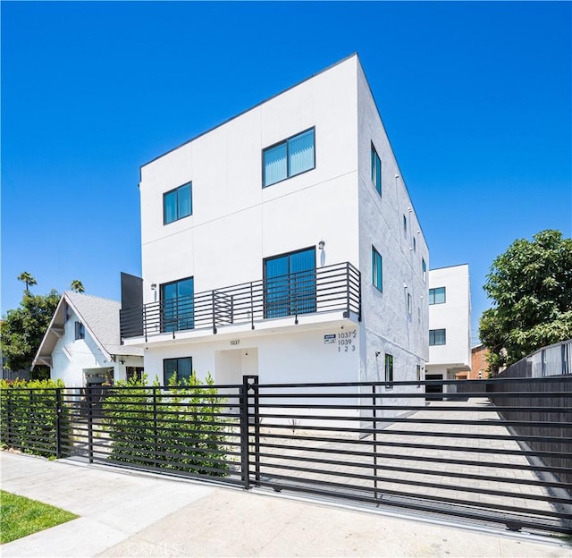 contemporary house featuring a balcony, a fenced front yard, and stucco siding