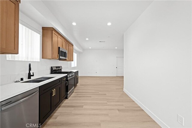 kitchen with recessed lighting, light wood-type flooring, baseboards, a sink, and appliances with stainless steel finishes