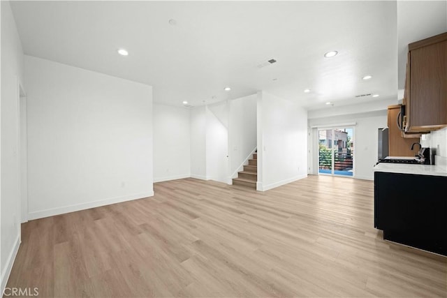 unfurnished living room with stairs, light wood-style flooring, and recessed lighting