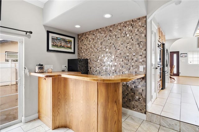 bar featuring recessed lighting, arched walkways, baseboards, a bar, and light tile patterned flooring