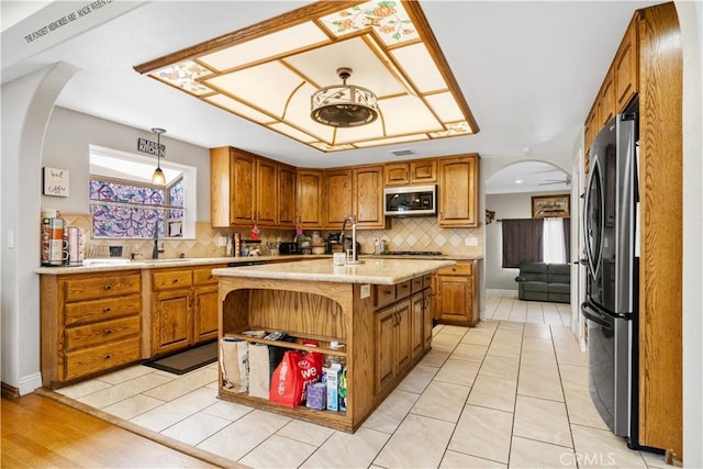 kitchen featuring arched walkways, stainless steel appliances, light countertops, brown cabinets, and a sink