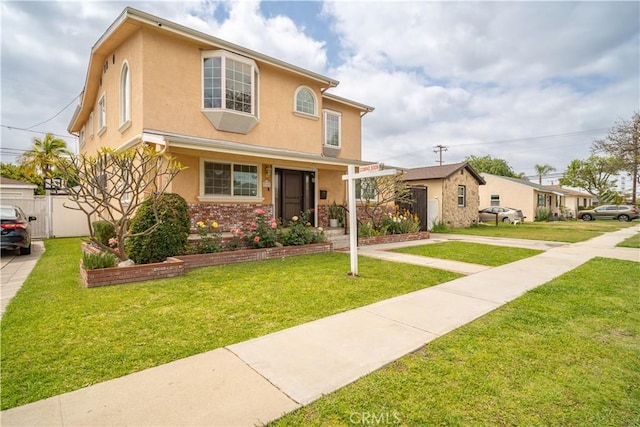 traditional-style home featuring stucco siding, fence, and a front lawn