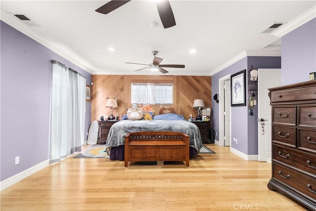 bedroom with light wood-style flooring, wood walls, baseboards, visible vents, and crown molding