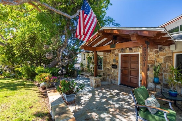 view of exterior entry with a patio, a yard, and stone siding