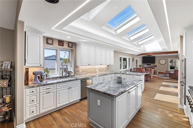 kitchen featuring a skylight, stainless steel dishwasher, a sink, a peninsula, and white cabinetry