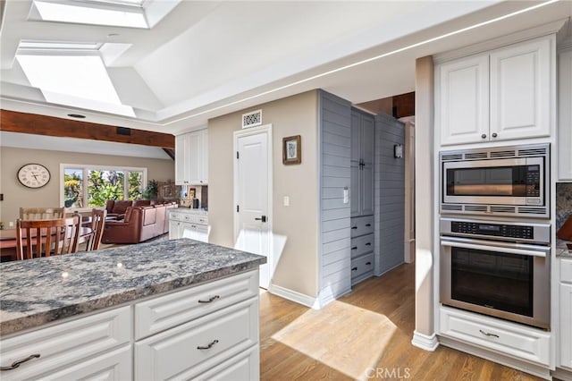 kitchen featuring white cabinets, appliances with stainless steel finishes, stone counters, and light wood-style flooring