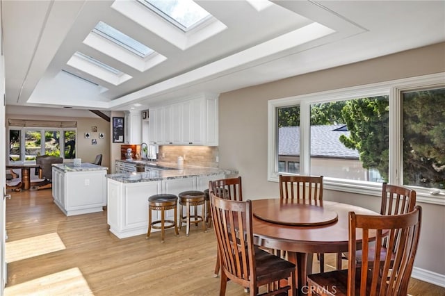 dining space with a skylight, a tray ceiling, and light wood-style floors