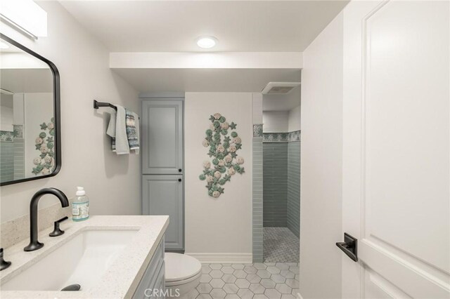 bathroom featuring toilet, a tile shower, and vanity