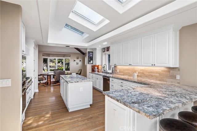 kitchen featuring white cabinets, a tray ceiling, stainless steel dishwasher, a skylight, and a kitchen island