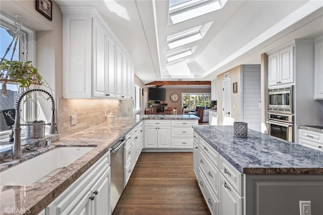 kitchen featuring appliances with stainless steel finishes, a sink, vaulted ceiling with skylight, white cabinetry, and decorative backsplash