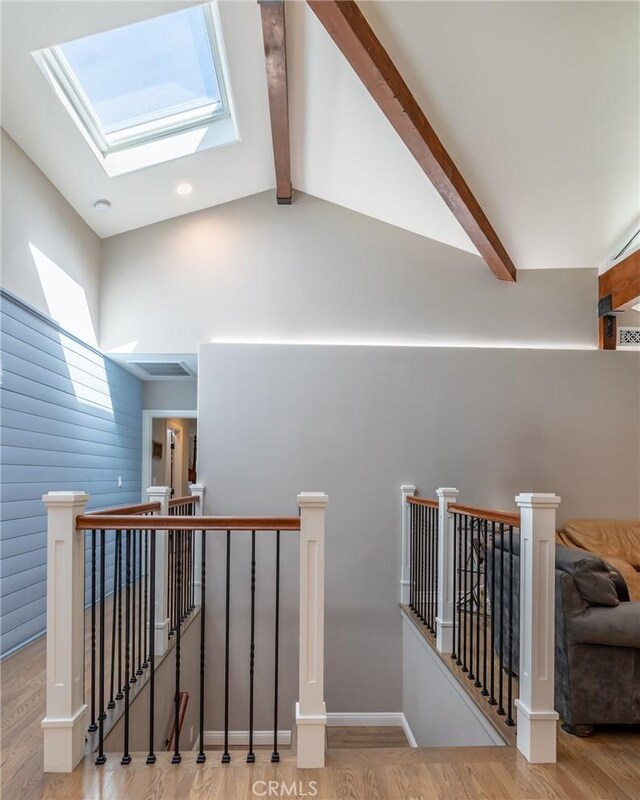 corridor with lofted ceiling with skylight, wood finished floors, and an upstairs landing