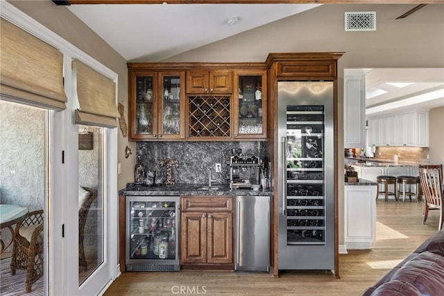 bar featuring stainless steel refrigerator, visible vents, indoor wet bar, wine cooler, and vaulted ceiling