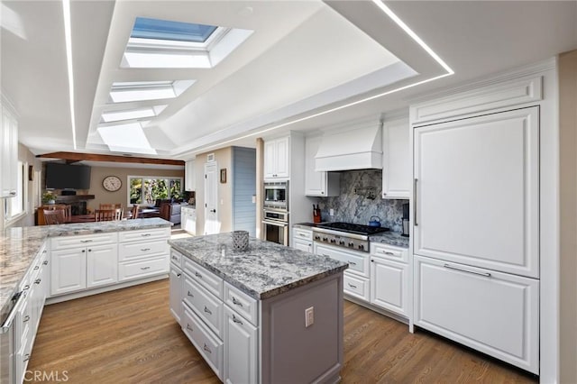 kitchen with custom range hood, white cabinetry, a skylight, and stainless steel appliances
