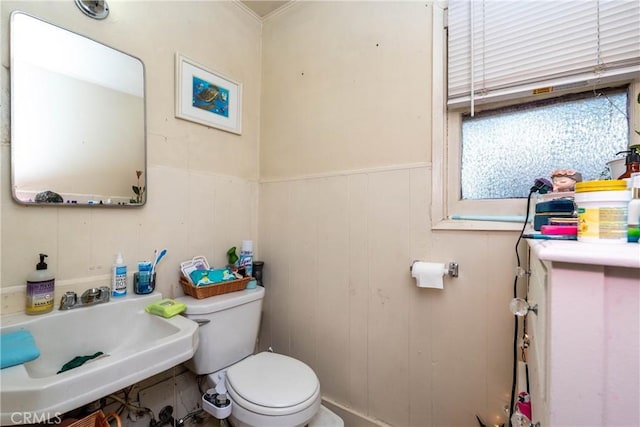 half bath featuring toilet, a wainscoted wall, and a sink