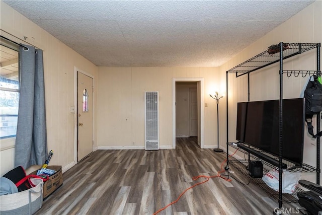 unfurnished living room with wood finished floors, a textured ceiling, baseboards, and a heating unit