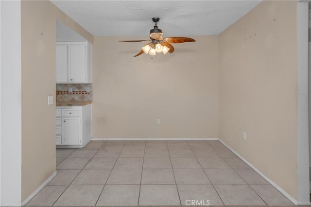 unfurnished dining area with a ceiling fan, light tile patterned floors, baseboards, and a textured ceiling