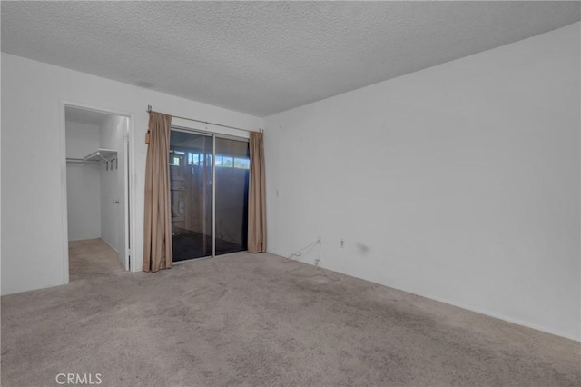 unfurnished bedroom with a walk in closet, a closet, carpet flooring, and a textured ceiling