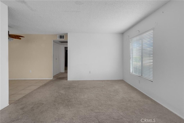 carpeted spare room featuring visible vents, tile patterned flooring, and a textured ceiling