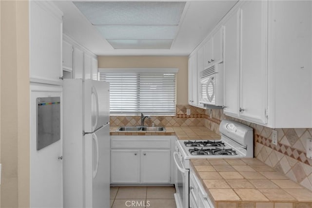 kitchen featuring white cabinets, tile counters, white appliances, a sink, and light tile patterned floors