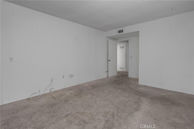 carpeted empty room featuring a textured ceiling and visible vents