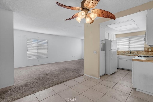 kitchen featuring tile countertops, a sink, open floor plan, freestanding refrigerator, and light colored carpet