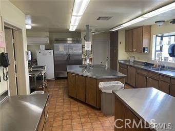 kitchen with stainless steel built in fridge, freestanding refrigerator, visible vents, a kitchen island, and light tile patterned flooring