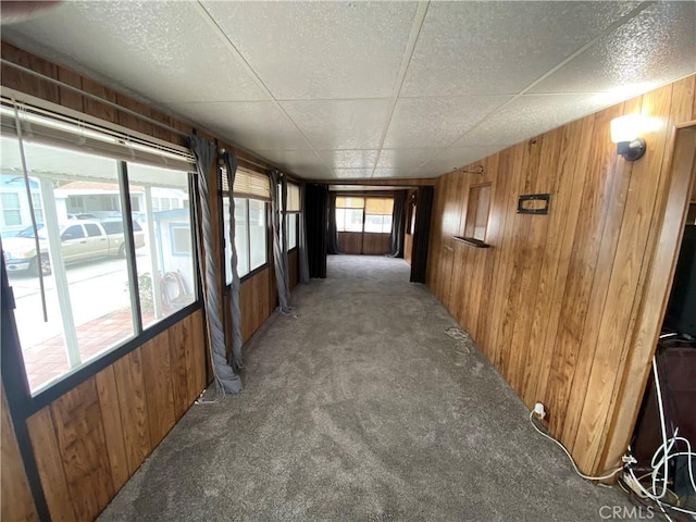 corridor with light colored carpet, wood walls, and a paneled ceiling