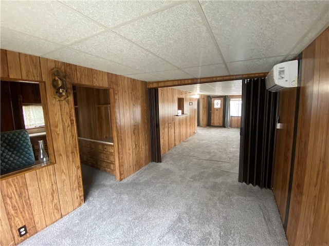 hallway with a drop ceiling, carpet flooring, wood walls, and a wall mounted AC