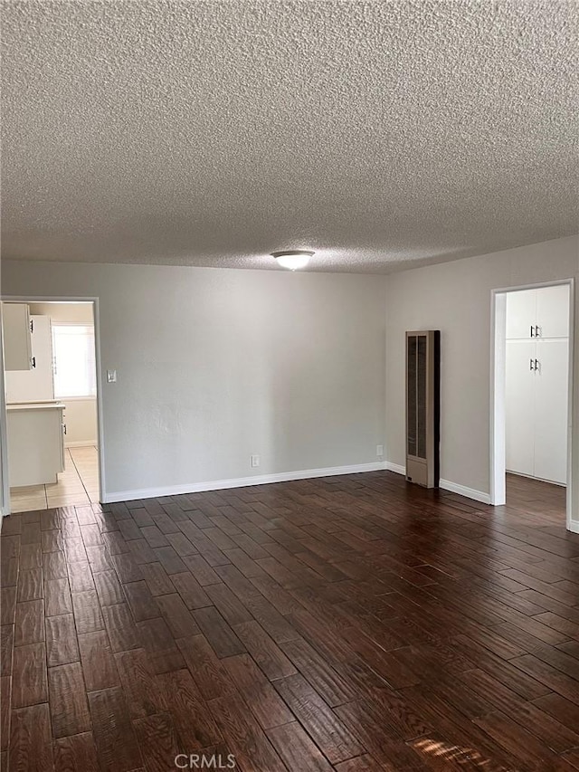 empty room with baseboards, a textured ceiling, and dark wood finished floors