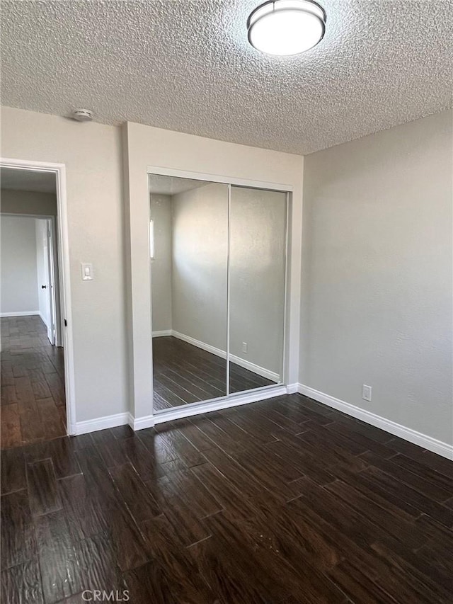 unfurnished bedroom with dark wood-style floors, a closet, a textured ceiling, and baseboards