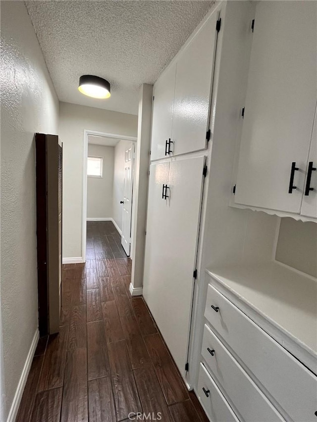 hall with a textured ceiling, baseboards, and wood tiled floor