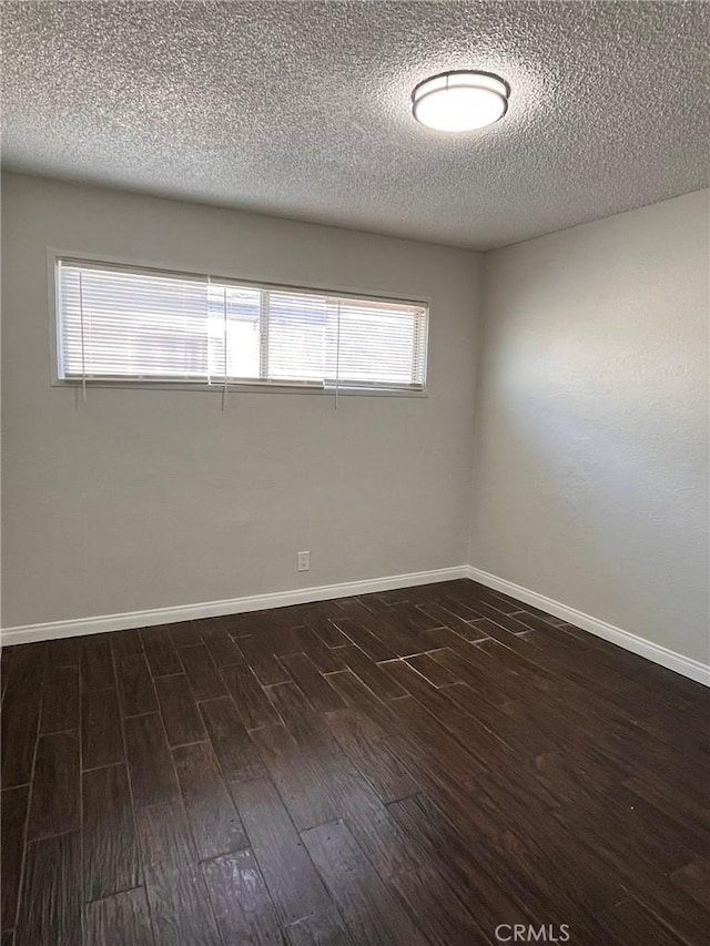 empty room featuring baseboards, a textured ceiling, and dark wood-style flooring
