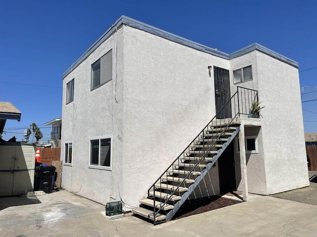 back of house featuring fence, a shed, stucco siding, and an outdoor structure