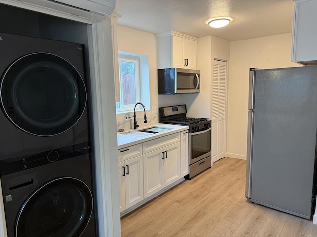 kitchen featuring white cabinetry, light countertops, stacked washer and clothes dryer, stainless steel appliances, and a sink