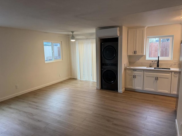 interior space with stacked washer / drying machine, a sink, wood finished floors, laundry area, and baseboards