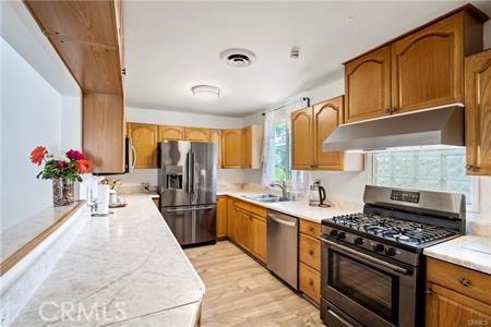 6927 Lindley Ave, Reseda, CA 91335 - kitchen with appliances with stainless steel finishes, under cabinet range hood, light countertops, light wood-style floors, and brown cabinetry