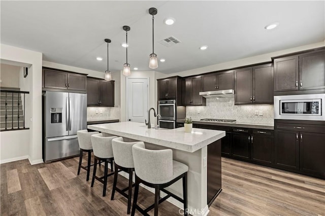 kitchen featuring stainless steel appliances, under cabinet range hood, light wood finished floors, and visible vents