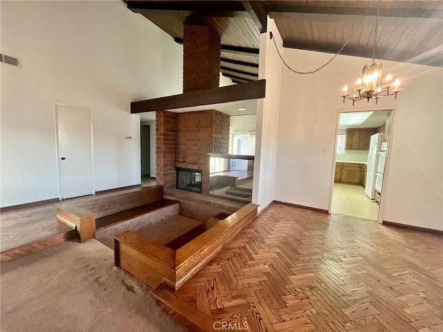 unfurnished living room featuring high vaulted ceiling, visible vents, a brick fireplace, baseboards, and a notable chandelier