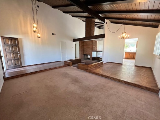 unfurnished living room featuring an inviting chandelier, a fireplace, carpet flooring, beam ceiling, and wooden ceiling