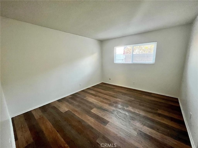 unfurnished room featuring baseboards and dark wood finished floors