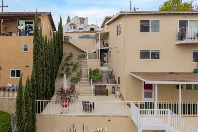 rear view of house with stairs, stucco siding, fence, and a patio area