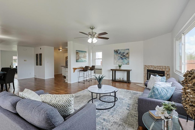 living area featuring wood finished floors, a tile fireplace, and ceiling fan