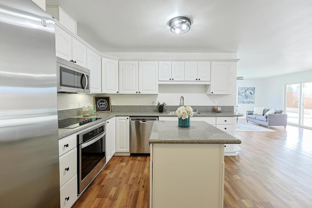 kitchen featuring white cabinets, stainless steel appliances, a sink, a kitchen island, and light wood-style flooring