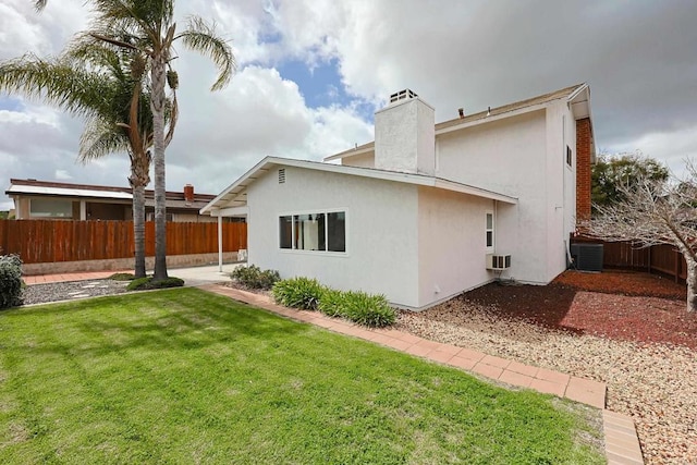 back of house with a lawn, a chimney, a fenced backyard, and stucco siding