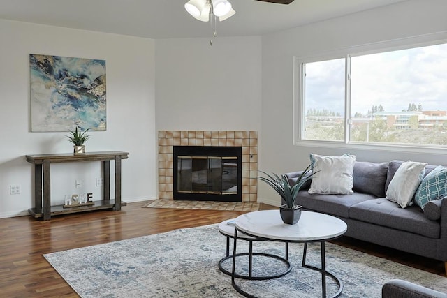 living room with wood finished floors, a tiled fireplace, a ceiling fan, and baseboards