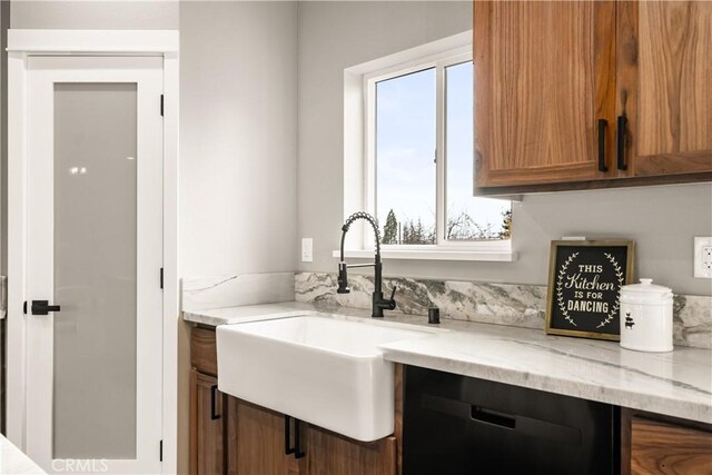 kitchen featuring brown cabinetry, light stone counters, black dishwasher, and a sink