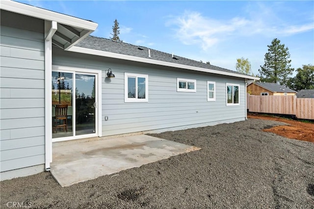 back of property with fence, a patio area, and a shingled roof
